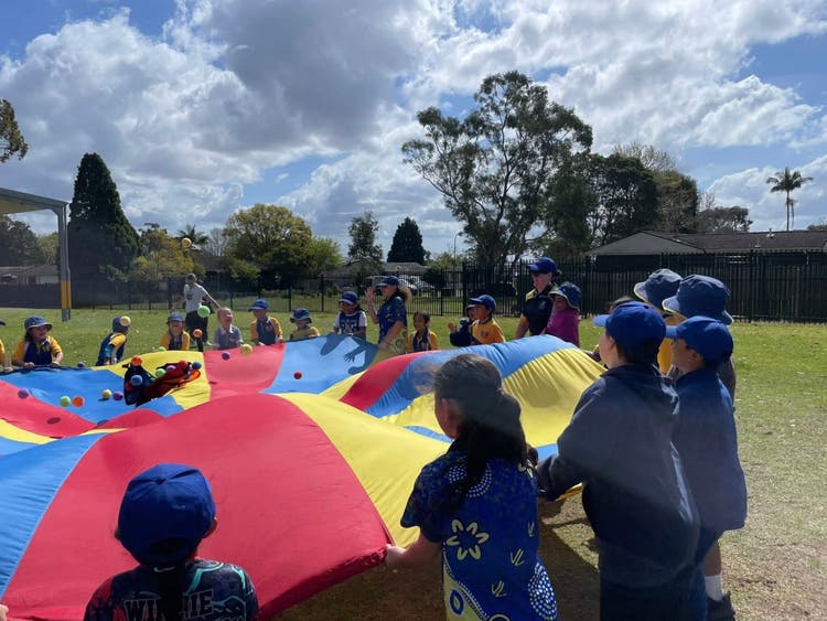 Children joyfully playing with a colorful parachute in a sunny park.